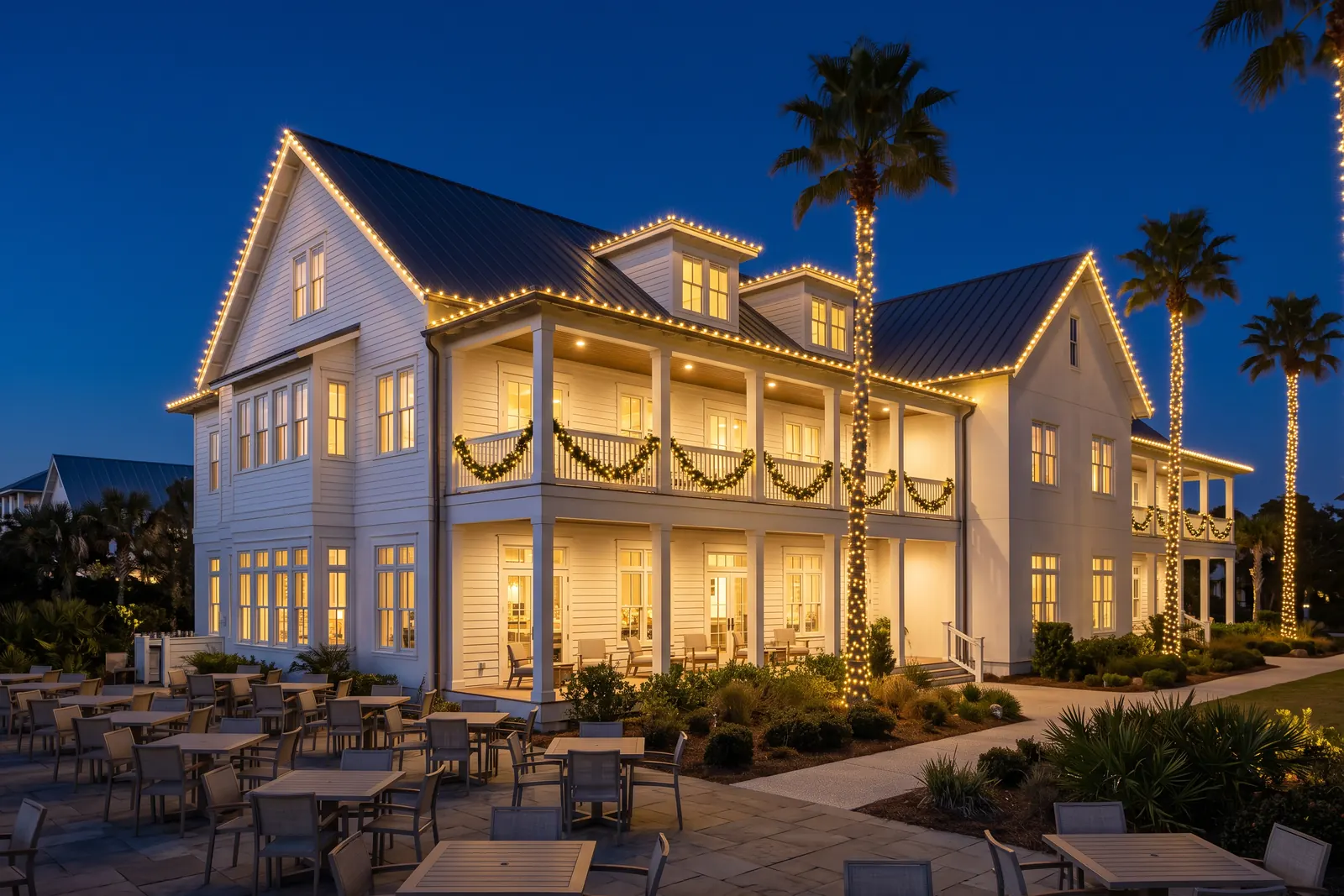 Coastal inn with warm-white roofline, veranda garland and lit palms, design concept